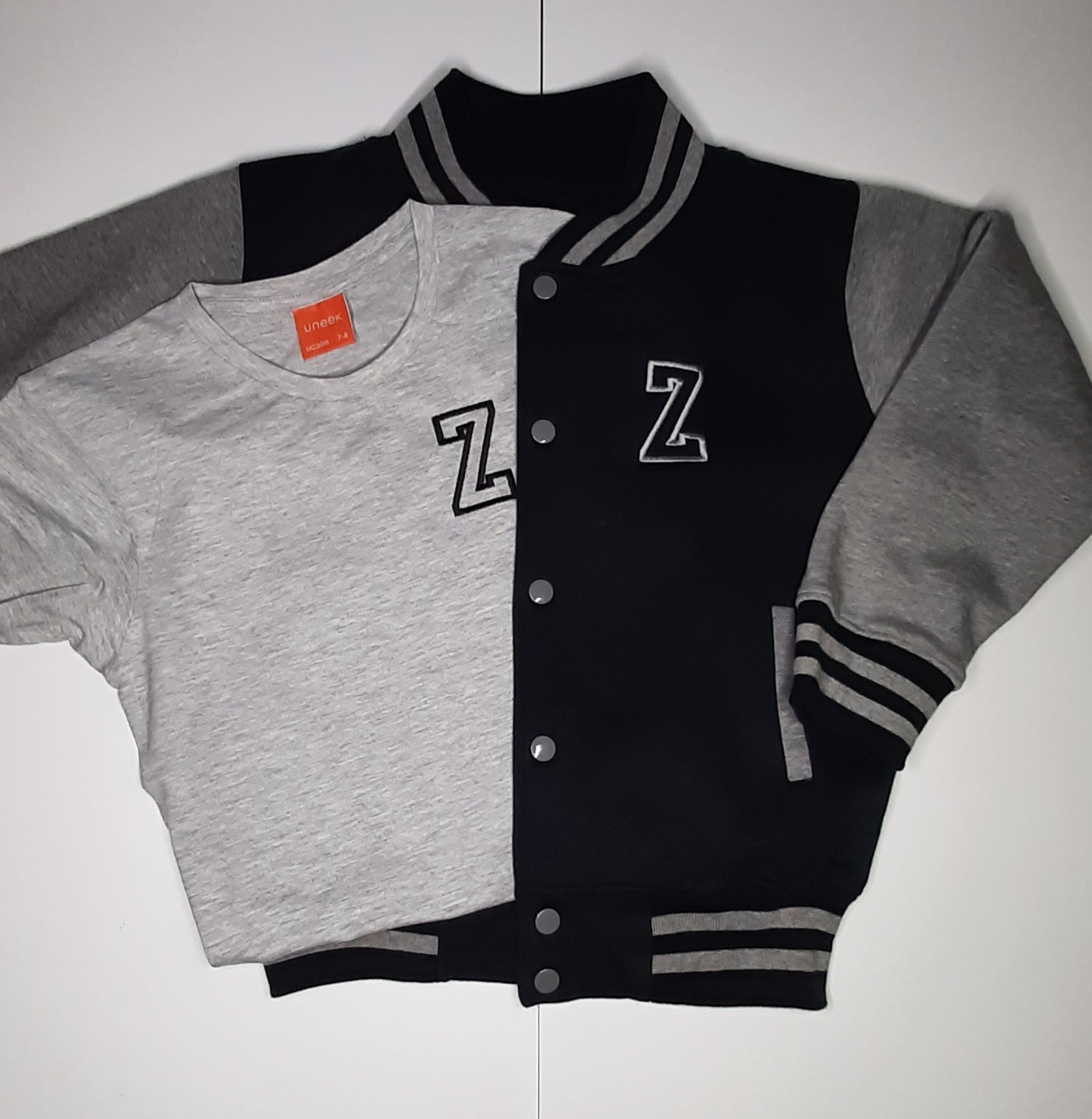 Children's varsity jacket on model in black and grey with embroidered initial laid with matching t shirt