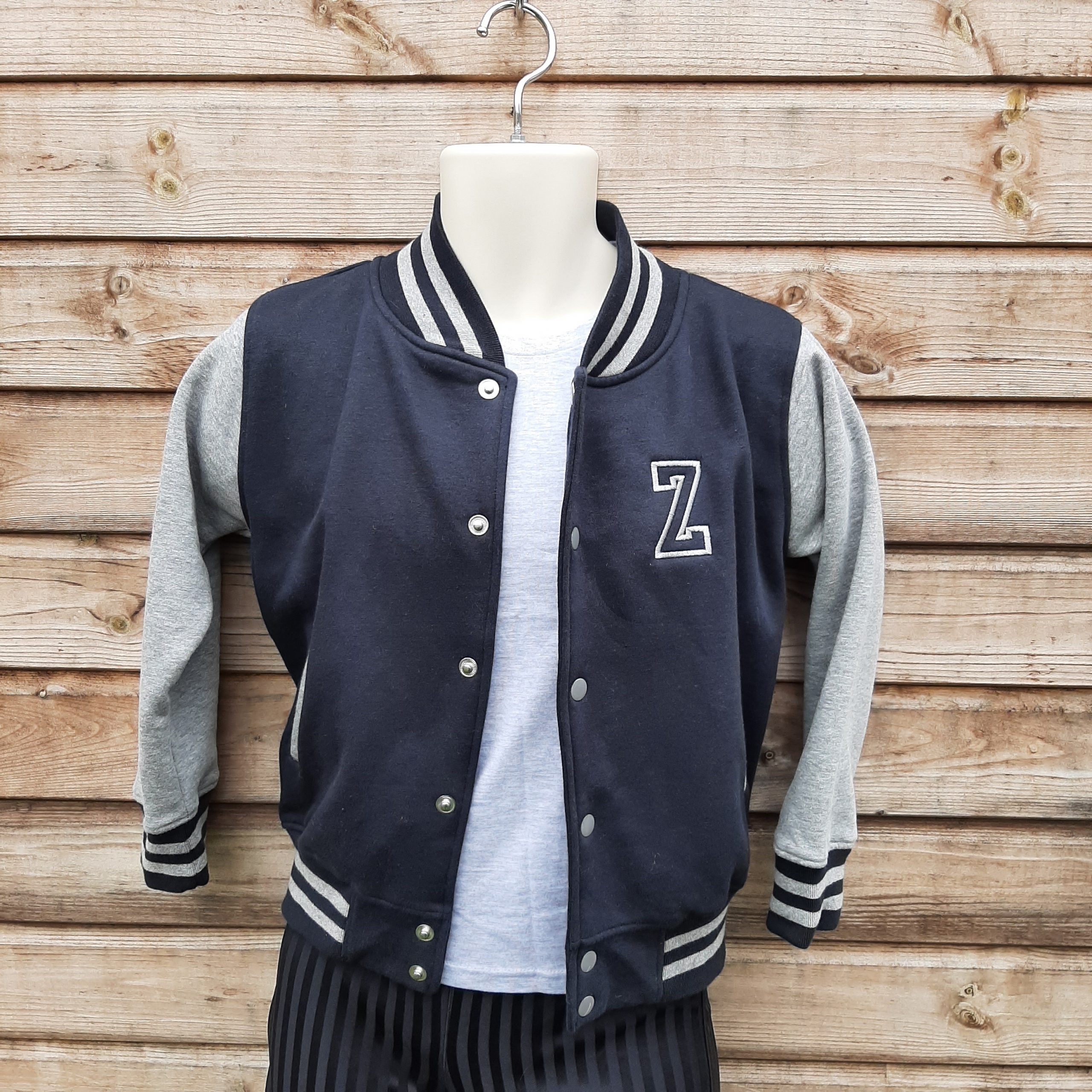 Children's varsity jacket on model in black and grey with embroidered initial hung up