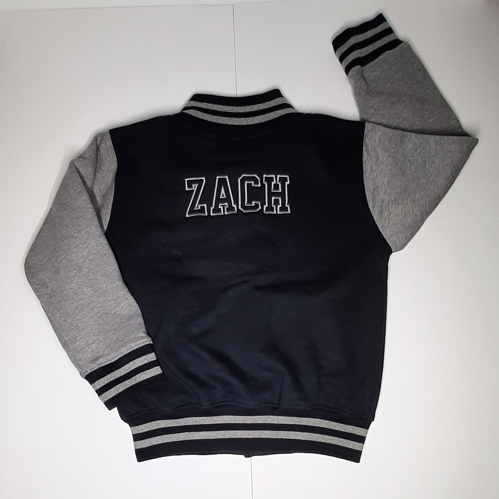 Children's varsity jacket on model in black and grey with embroidered name laid out