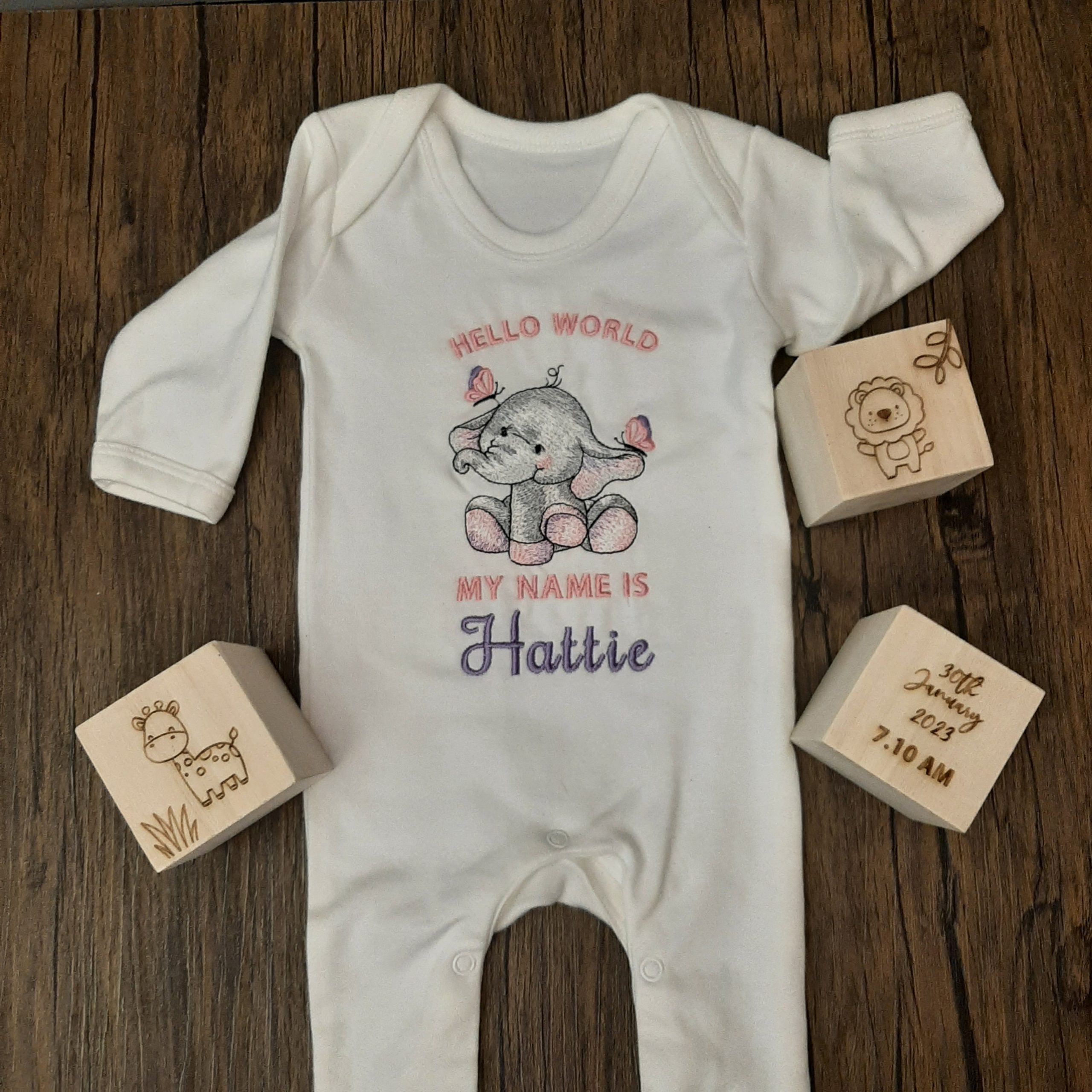 baby sleepsuit hello world embroidery design laid on floor, white romper with elephant personalised design announcement