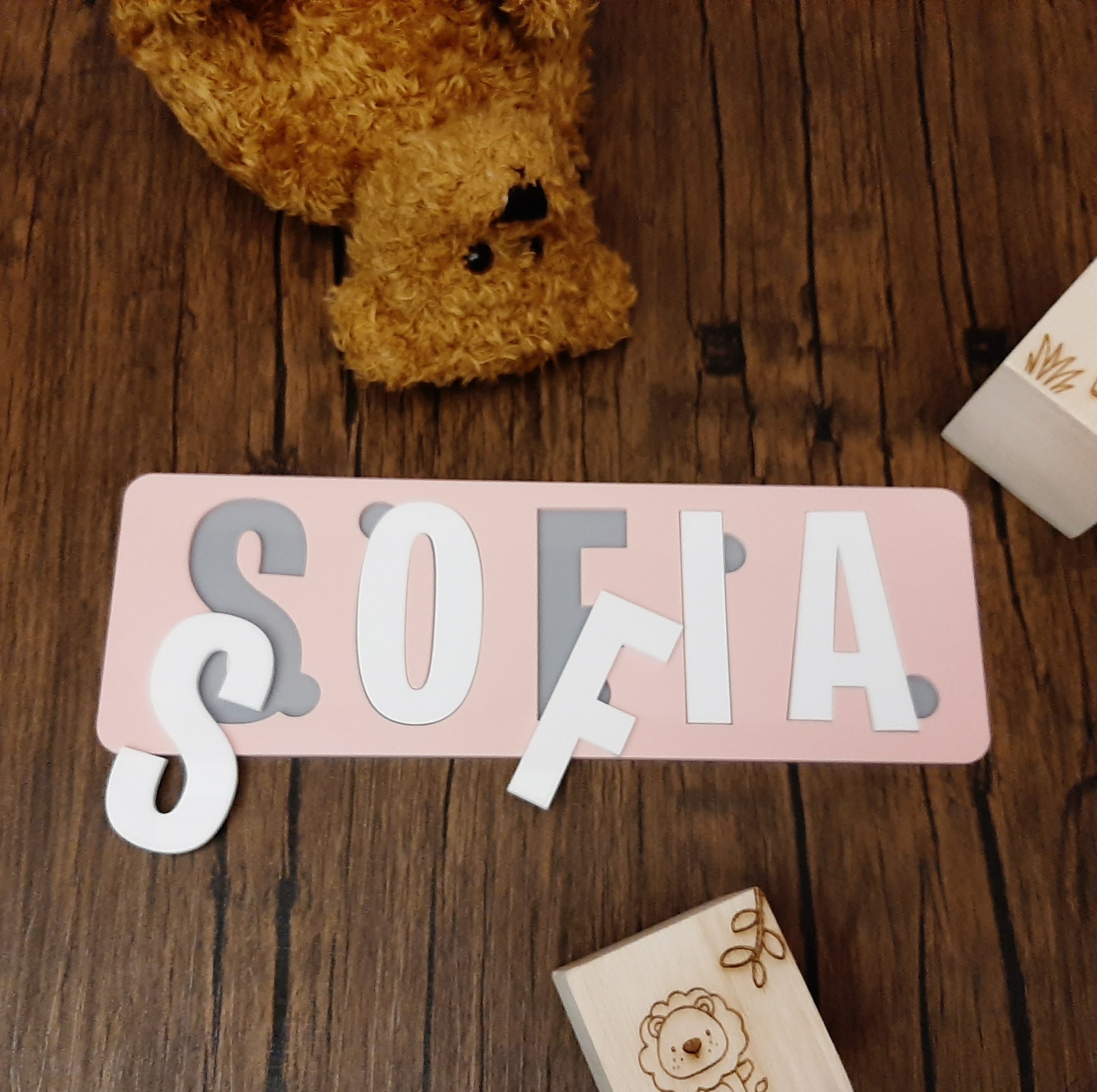 colourful name puzzle in pink white and grey laid on floor with teddy and blocks