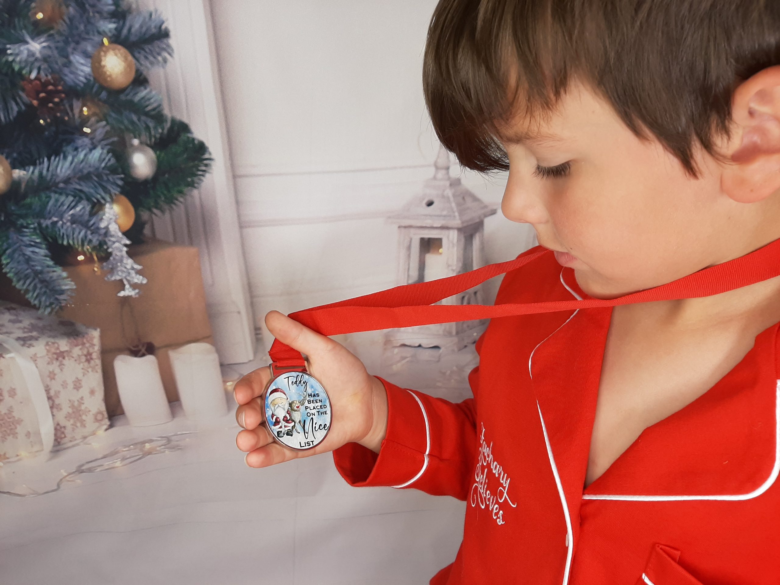 boy in christmas pjs holding a made the nice list medal with red ribbon personalised with childs name