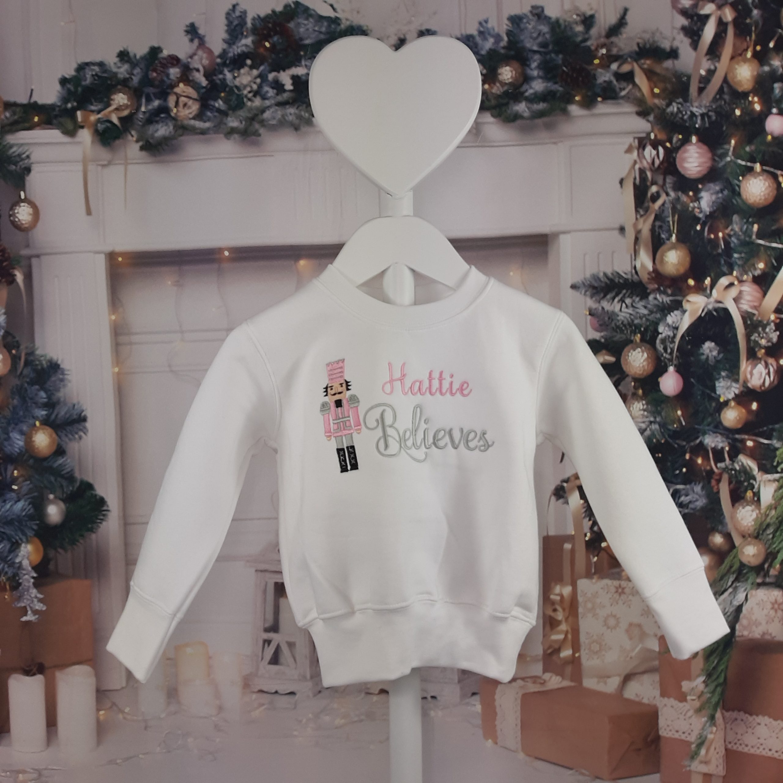 white Nutcracker Christmas Jumper in pink and silver, blue and silver or red and gold all personalised and professionally embroidered with name believes. hung up